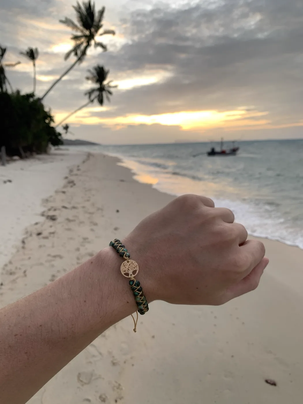 Bracelet Arbre de Vie doré porté au poignet face à la mer au coucher du soleil